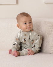 Load image into Gallery viewer, A baby sitting on a textured cream sofa wearing a sage green long-sleeve pajama with a whimsical print of witches, cauldrons, and stars.
