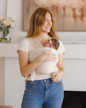 Load image into Gallery viewer, Woman holding a newborn baby in a home setting with a painting and flowers in the background.
