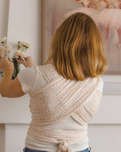 Load image into Gallery viewer, A woman viewed from behind wearing a cream and beige patterned wrap-style top or dress, standing indoors near a vase of flowers and a framed ballet scene on the wall.
