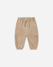 Load image into Gallery viewer, Latte tan pants with an elastic drawstring waist, two front buttons, large patch pockets, and elastic ankle cuffs.
