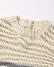 Load image into Gallery viewer, Close-up of a chunky knit crewneck sweater in cream with a gray stripe detail at the bottom hem, showing the ribbed collar and a small interior brand label.
