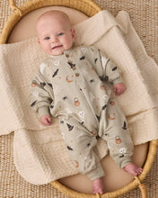 Load image into Gallery viewer, A baby lying on a cream textured blanket inside a woven basket, wearing a light beige footless sleeper with a Halloween print of ghosts, bats, pumpkins, and moons.
