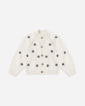 Load image into Gallery viewer, An off-white knit cardigan sweater with small dark gray embroidered snowflake motifs and brown buttons, displayed flat against a light gray background.
