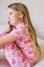 Load image into Gallery viewer, Young girl wearing a pink and orange patterned shirt sitting on a white couch.
