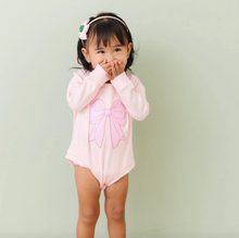 Load image into Gallery viewer, Child wearing a pink swimsuit with a large bow on a light green background
