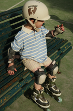 Load image into Gallery viewer, Child sitting on a bench wearing roller skates and protective gear, with a helmet.
