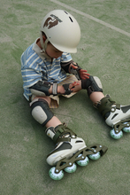 Load image into Gallery viewer, Child sitting on a grassy surface wearing roller skates, knee pads, and a helmet.
