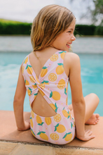 Load image into Gallery viewer, Young girl in a lemon-patterned swimsuit sitting by a pool.
