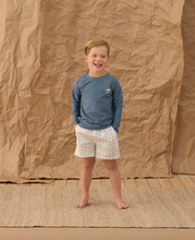 Load image into Gallery viewer, Child wearing a blue shirt and patterned shorts standing against a brown paper backdrop

