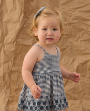 Load image into Gallery viewer, Young child wearing a blue checkered dress against a brown textured background
