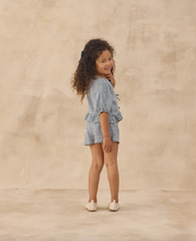 Load image into Gallery viewer, Young girl wearing a blue checkered outfit against a beige background
