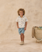 Load image into Gallery viewer, Child wearing a collared shirt and shorts standing on a beige background
