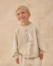Load image into Gallery viewer, Child wearing a beige sweatshirt with a sailboat design on a plain background
