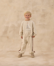 Load image into Gallery viewer, Child wearing a beige sweatshirt and pants set with a sailboat design on a beige background
