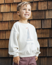 Load image into Gallery viewer, Child wearing a white sweatshirt with a sailboat design in front of a wooden wall.

