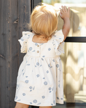 Load image into Gallery viewer, Child wearing a white dress with blue patterns, standing near a wooden door.
