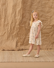 Load image into Gallery viewer, Young girl in a dress standing against a textured brown background
