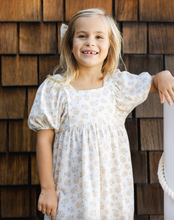 Load image into Gallery viewer, Young girl in a floral dress standing against a wooden wall.
