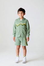 Load image into Gallery viewer, Child wearing a green hoodie and shorts set with white sneakers on a light background
