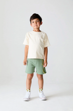 Load image into Gallery viewer, Child wearing a white t-shirt and green shorts on a white background
