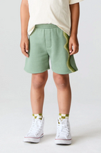 Load image into Gallery viewer, Person wearing green shorts with white high-top sneakers on a plain background
