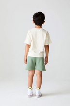 Load image into Gallery viewer, Child wearing a white t-shirt and green shorts on a plain background
