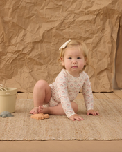 Load image into Gallery viewer, Child in a floral onesie sitting on a textured surface with a brown paper bag background

