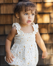 Load image into Gallery viewer, Child wearing a white  romper standing against a wooden wall.
