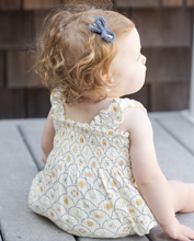 Load image into Gallery viewer, Young child wearing a romper sitting on a wooden floor.
