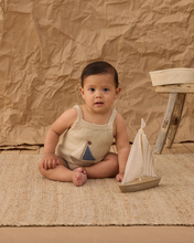 Load image into Gallery viewer, Baby sitting on a textured rug with a wooden sailboat, against a brown paper backdrop.
