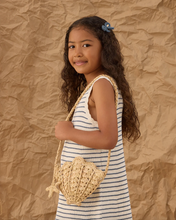 Load image into Gallery viewer, Young girl in a striped dress holding a woven shell bag against a textured brown background

