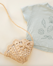 Load image into Gallery viewer, Light blue t-shirt with shell designs and a woven bag on a beige background
