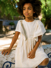 Load image into Gallery viewer, Young girl in a white dress sitting outdoors with greenery in the background

