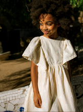 Load image into Gallery viewer, Young girl in a white dress standing outdoors with a blurred background

