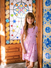 Load image into Gallery viewer, Young girl in a pink dress standing in front of a stained glass window and decorative wall.
