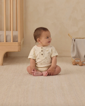 Load image into Gallery viewer, Baby sitting on a beige carpeted floor next to a wooden crib.
