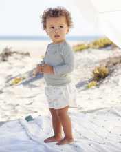 Load image into Gallery viewer, Child standing on a sandy beach wearing a light gray long-sleeve shirt and white shorts.
