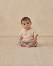 Load image into Gallery viewer, Baby sitting on a beige surface wearing a white shirt and gray pants.
