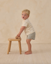 Load image into Gallery viewer, Child standing next to a small wooden stool on a beige background
