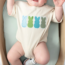 Load image into Gallery viewer, Baby wearing a onesie with colorful bunny designs on a light green surface.
