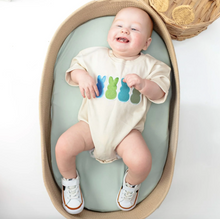 Load image into Gallery viewer, Baby sitting in a green and beige oval seat with a colorful onesie.
