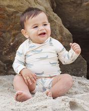 Load image into Gallery viewer, Baby sitting on sand wearing a patterned onesie with rocks in the background
