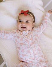 Load image into Gallery viewer, Baby wearing a white onesie with pink patterns and a red bow, sitting on a white cushion.
