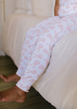 Load image into Gallery viewer, Person wearing light pink pajama pants with a subtle pattern, sitting on a white couch.
