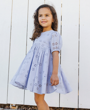 Load image into Gallery viewer, Young girl wearing a light blue dress with floral patterns against a white wooden fence.
