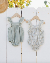 Load image into Gallery viewer, Two baby rompers on hangers against a white wooden fence with blurred greenery in the background.
