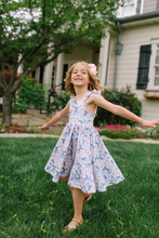 Load image into Gallery viewer, Young girl in a floral dress standing on grass with a house in the background
