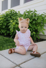 Load image into Gallery viewer, Child in a pink outfit sitting on a patio with greenery in the background
