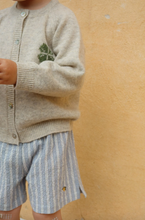 Load image into Gallery viewer, Child wearing a beige cardigan with a plant design and striped shorts against a yellow background
