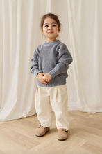 Load image into Gallery viewer, Child wearing a blue sweater and white pants standing in front of white curtains.

